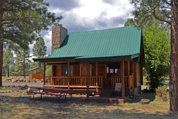 A cabin with green roof and picnic table in front.